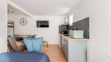 Un espace de vie compact comprenant un lit, un coin repas, une kitchenette et un téléviseur fixé au mur.