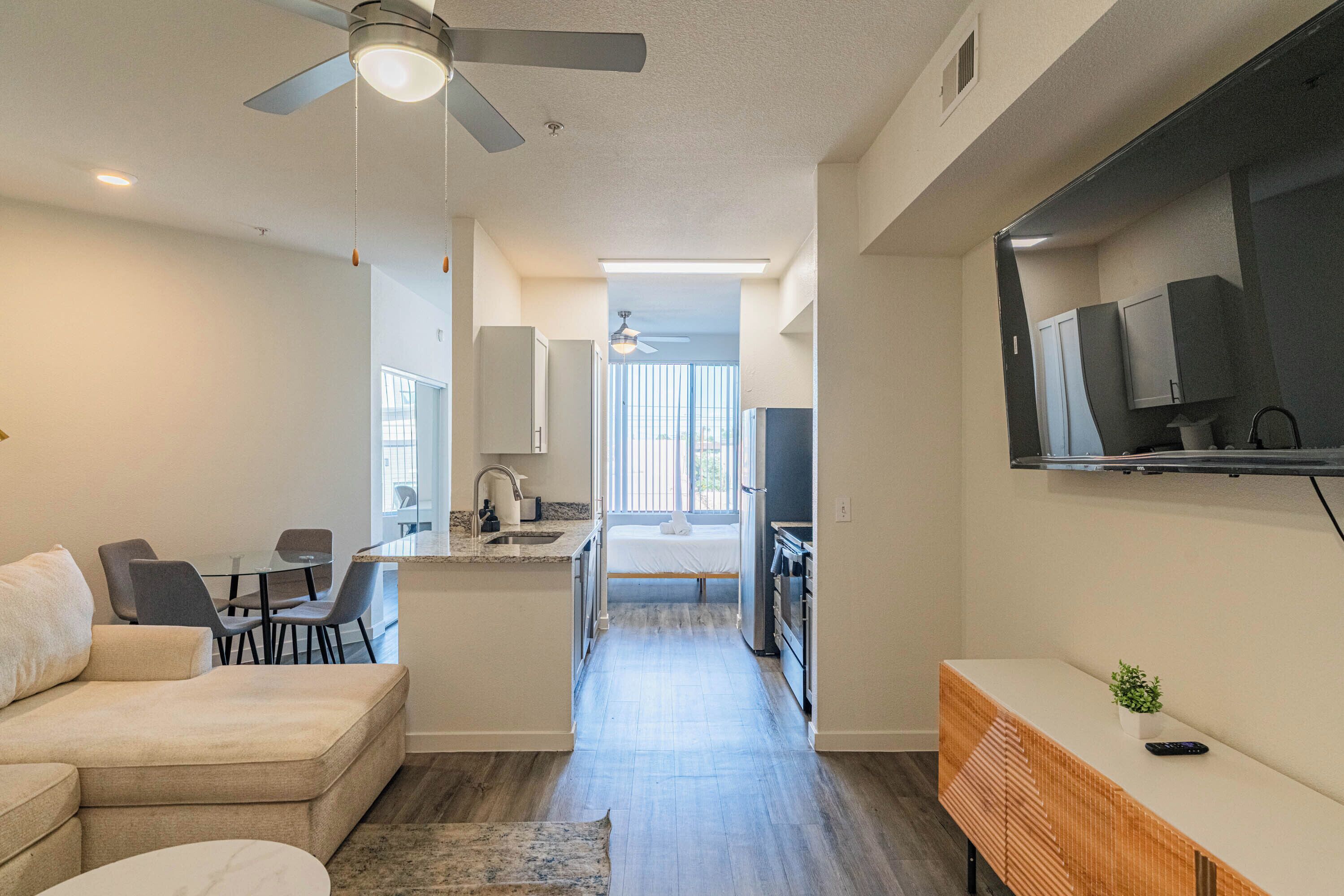 A compact living space with a kitchenette, a dining area, a sofa, and a TV mounted on the wall.