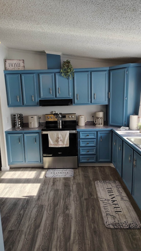 Une cuisine avec des armoires bleues, un poêle noir et un plancher en bois.