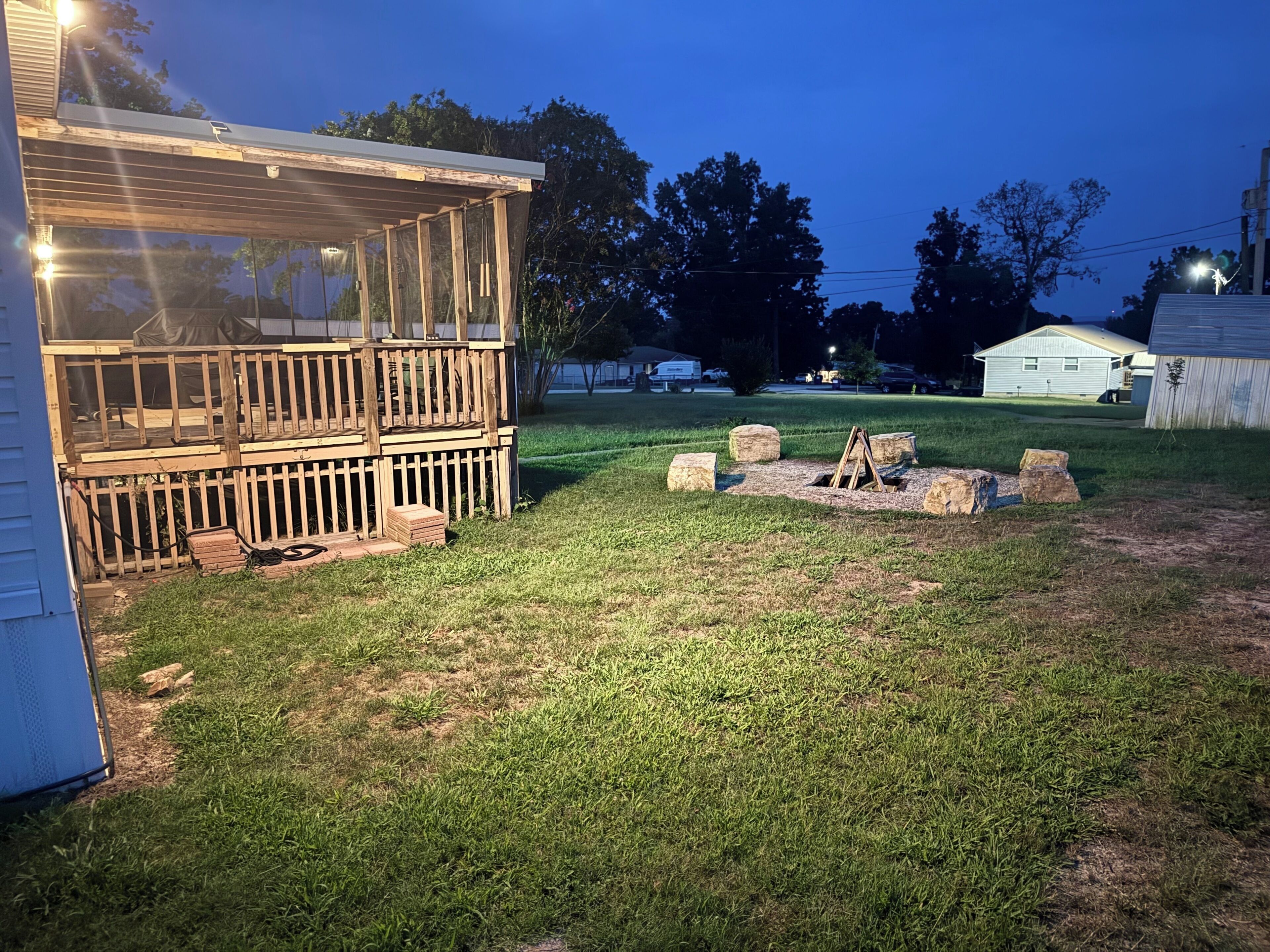 A wooden deck with a glass enclosure, a fire pit, and a grassy yard.