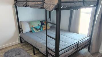 Ein Stockbett mit einem grauen, flauschigen Teppich, Holzboden und einem Fenster mit Vorhängen.