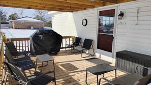 A covered patio with outdoor furniture, a grill, and a view of a house.