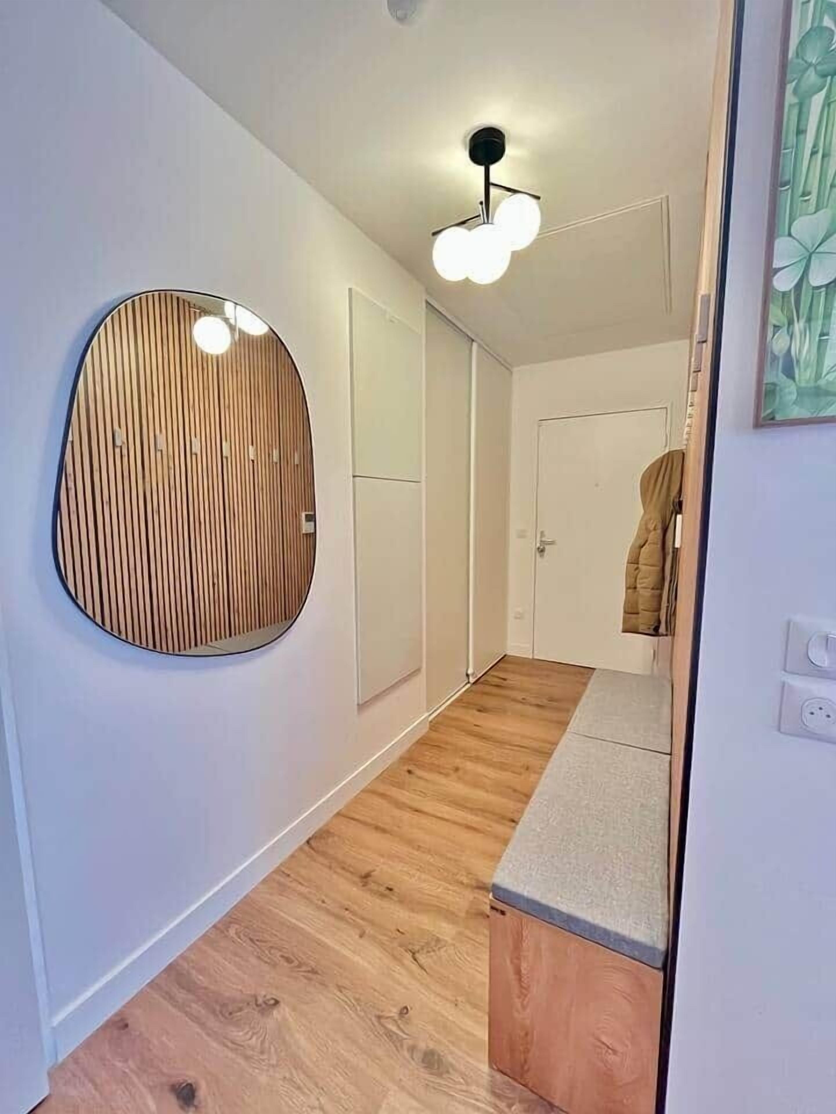Um corredor com painel de parede de madeira, luminária no teto e uma porta com um casaco pendurado.