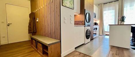 A modern kitchen with wooden cabinetry, a built-in washing machine, and a bench in the living area.