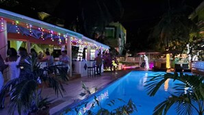 Zona de piscina exterior con bar y asientos, rodeada de plantas en macetas y palmeras.