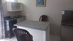 Una cocina compacta con estufa a gas, un lavamanos, una pequeña isla y dos sillas.
