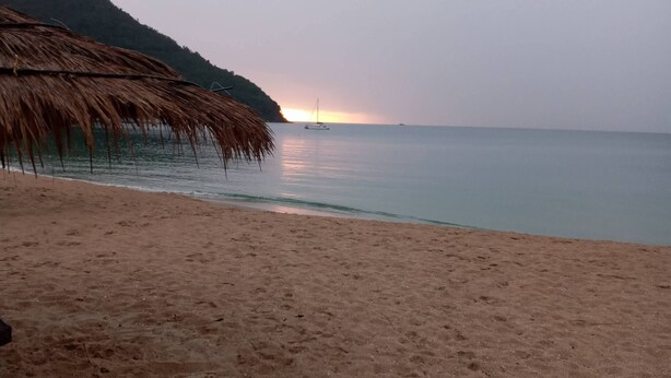 Una playa con una estructura de techo de paja y un mar tranquilo al atardecer.