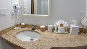 Une salle de bain équipée d’un lavabo avec un plan de toilette en granit, d’un sèche-cheveux, d’un miroir et d’articles de toilette.