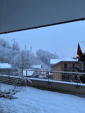 Blick aus einem Fenster auf eine verschneite Landschaft mit Bäumen und Häusern.
