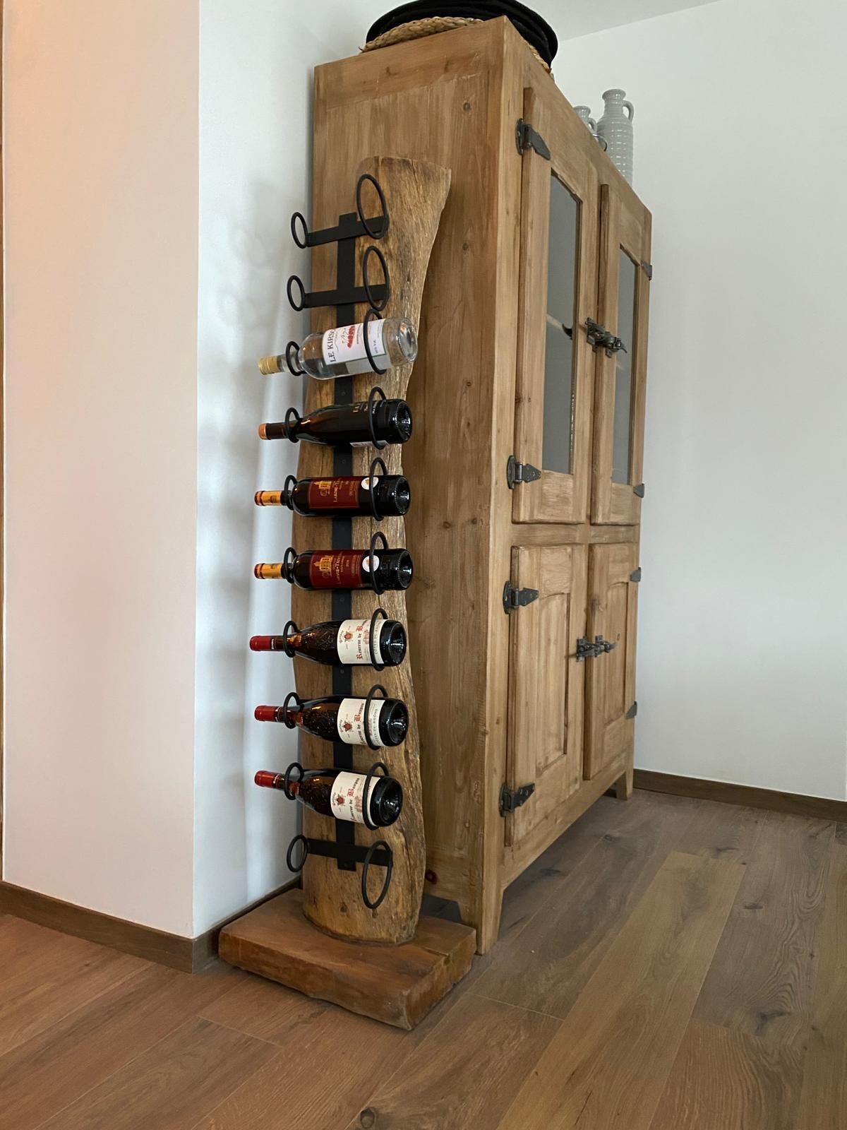 Ein Weinständer aus Holz mit Flaschen, an einer Wand, neben einem Holzschrank mit Glastüren.