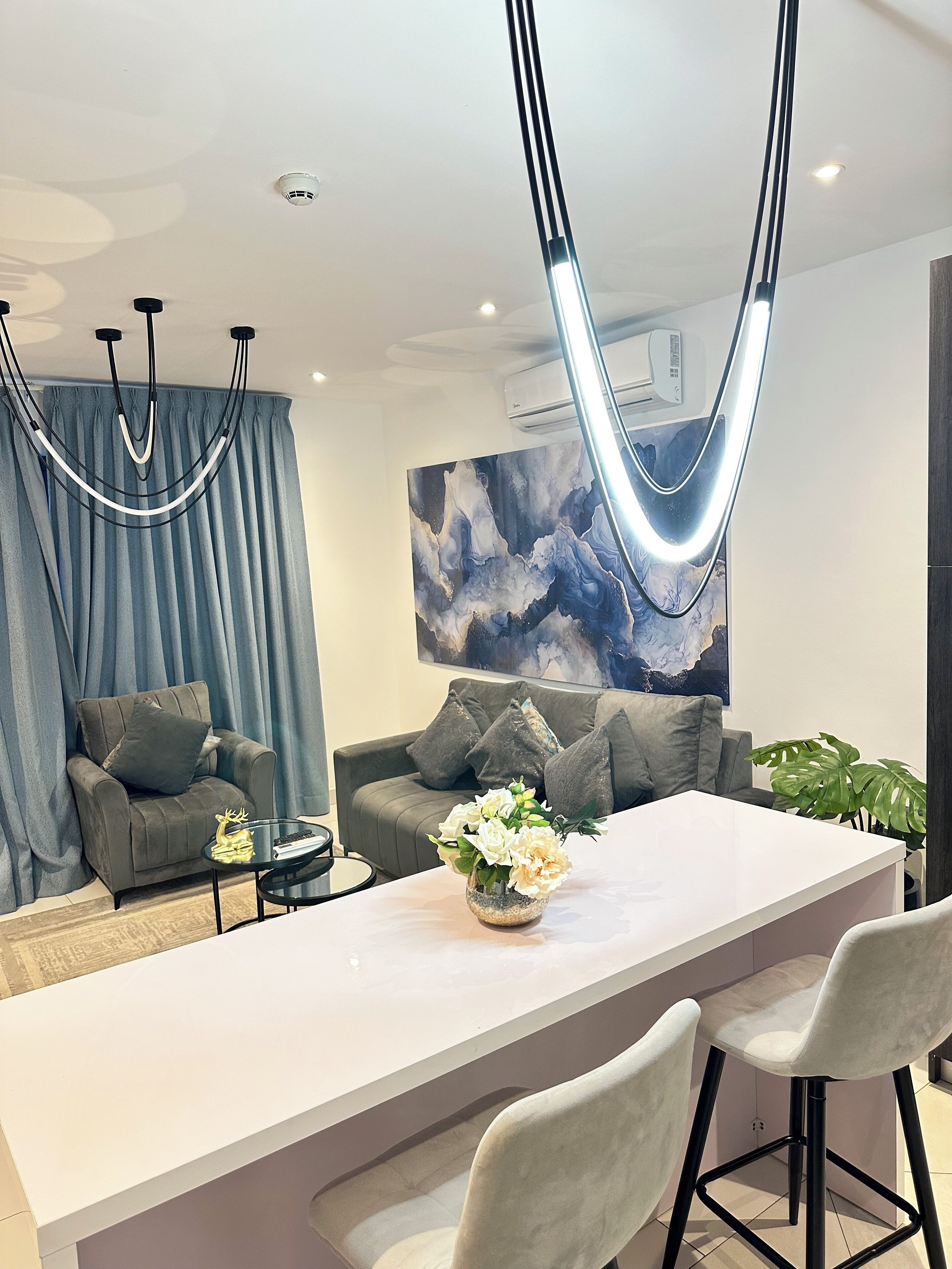 A modern living room with a white coffee table, grey sofas, and a large abstract painting on the wall.