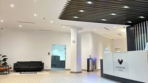 Un espace d’accueil moderne comprenant un comptoir de réception, un canapé noir et une plante.