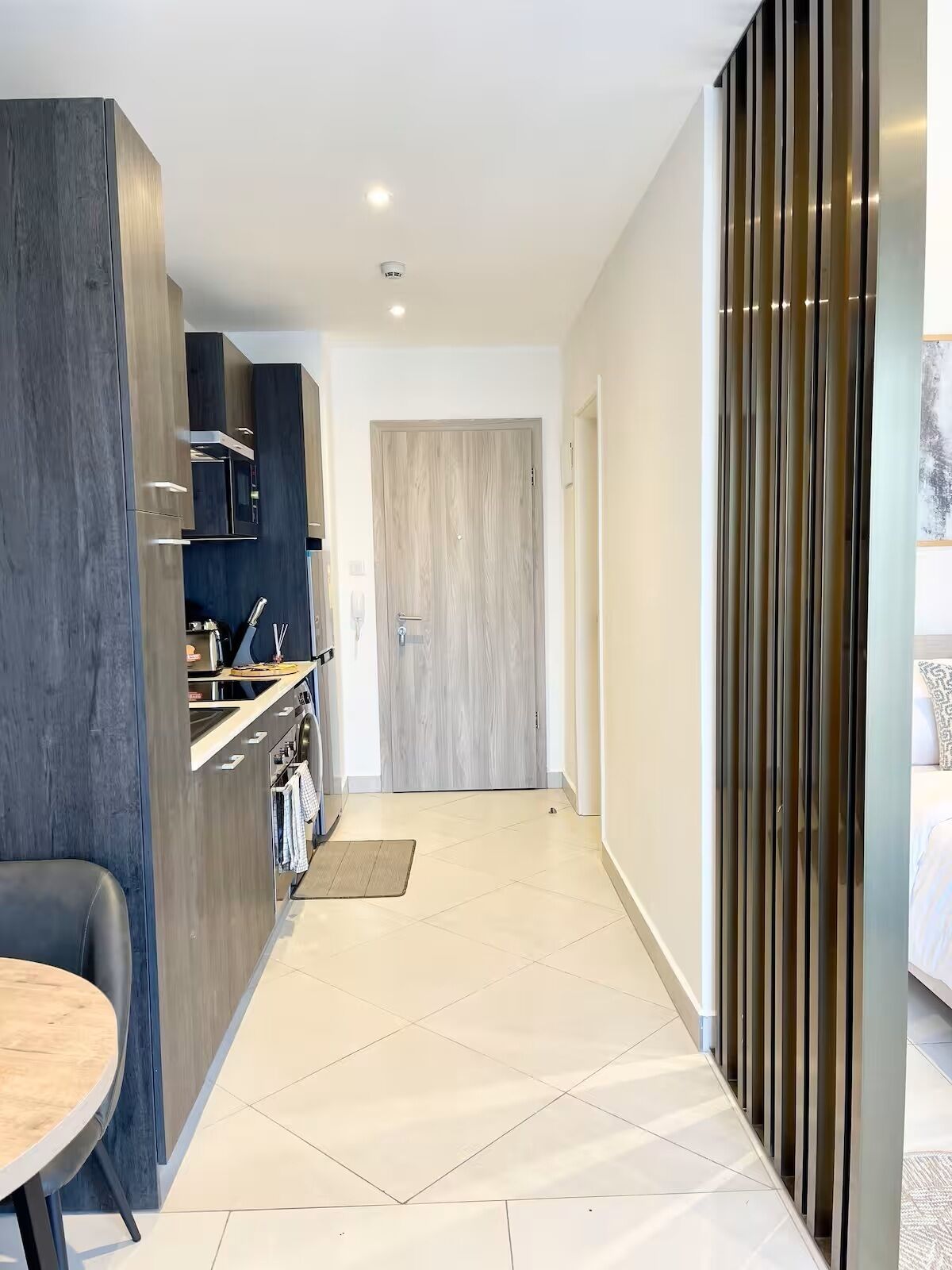 Eine moderne Küche mit dunklen Schränken, ein Essbereich mit Tisch und ein Schlafzimmer mit Bett und Fenster.