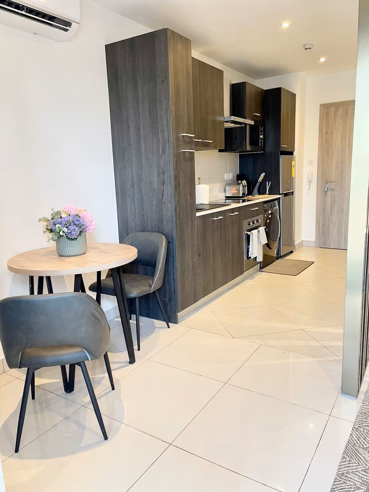 A modern kitchen with dark wood cabinets, stainless steel appliances, and a round dining table with two chairs.