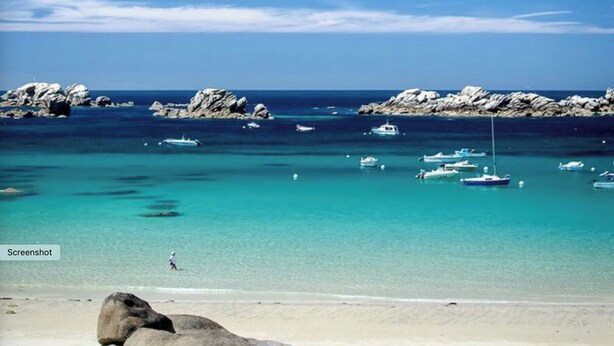 Een strand met helder turquoise water, rotsformaties en diverse boten die dichtbij de kust liggen aangemeerd.