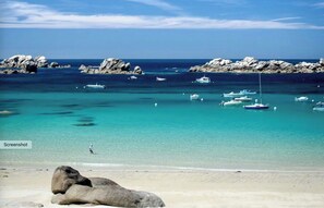 Une plage à l’eau turquoise et limpide, bordée de formations rocheuses, avec plusieurs bateaux ancrés près du rivage.