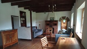 Een rustieke kamer met een houten eettafel, een bank, een open haard en een boekenkast.