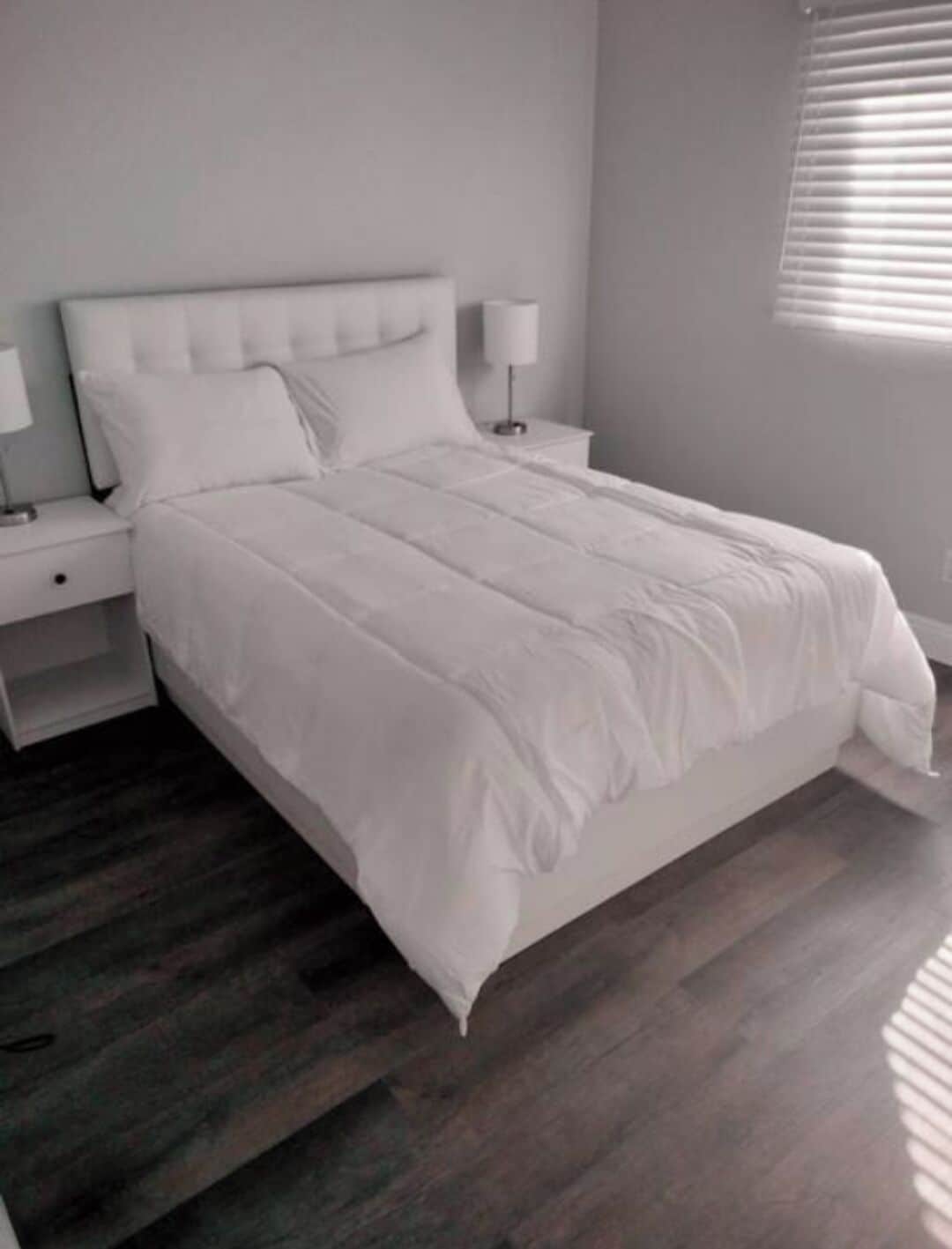 Un dormitorio moderno con una cama grande, ropa de cama blanca y suelo de madera.