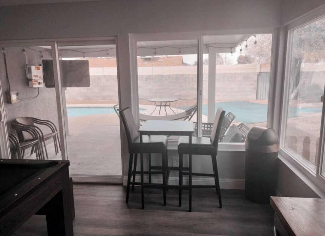 Una habitación con puerta de vidrio corrediza que da a un patio con piscina, mobiliario exterior y una mesa.