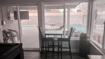Una habitación con puerta de vidrio corrediza que da a un patio con piscina, mobiliario exterior y una mesa.