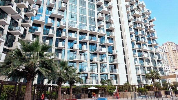 A modern hotel with a large pool area, featuring a unique architectural design with balconies and a clear blue sky. - Modern Deluxe Studio in Dubai (Al Jaddaf)