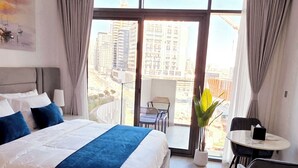 A hotel room with a large bed, a small table, and a view of the cityscape. - Modern Deluxe Studio in Dubai (Al Jaddaf)