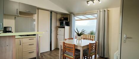 A compact kitchen with modern appliances, a dining area with wooden chairs, and a view through a large window.