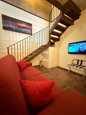 Ein Wohnzimmer mit einem roten Sofa, einer Treppe, einem Feuerlöscher und einem Fernseher.