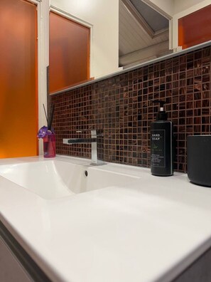 Ein Badezimmer mit einem weißen Waschbecken, einem schwarzen Handseifenspender und einer violetten Handseifenflasche.