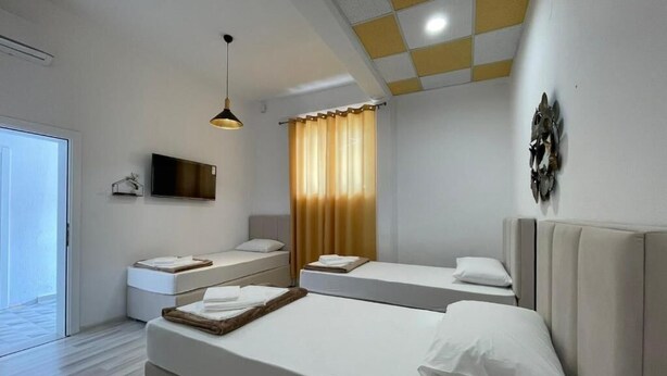 A modern hotel room with two beds, a flat-screen TV, a ceiling light, and a window with curtains. - HOSTEL IZVOR (Podgorica)