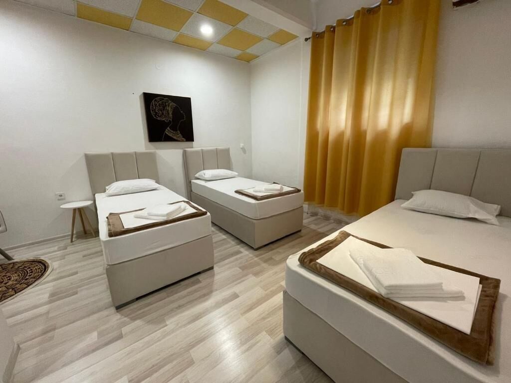 Habitación de hotel con dos camas individuales, una cama grande, una mesita pequeña y una obra de arte colgada en la pared.