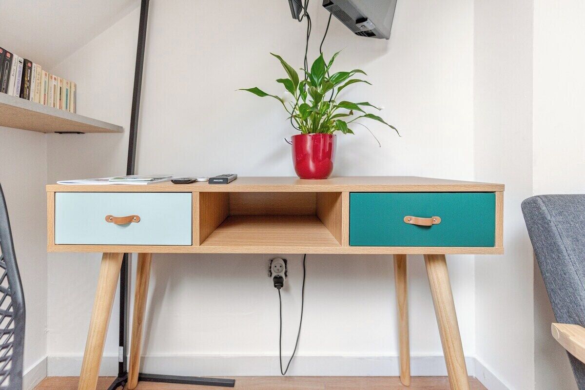 Een houten bureau met twee lades, een rode plant in een rode pot, en een plank met boeken.