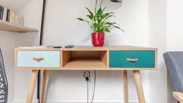 Een houten bureau met twee lades, een rode plant in een rode pot, en een plank met boeken.