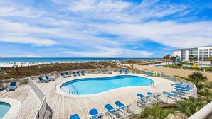 Ein Poolbereich mit Blick auf Strand und Meer, umgeben von Liegestühlen und einer Holzterrasse.