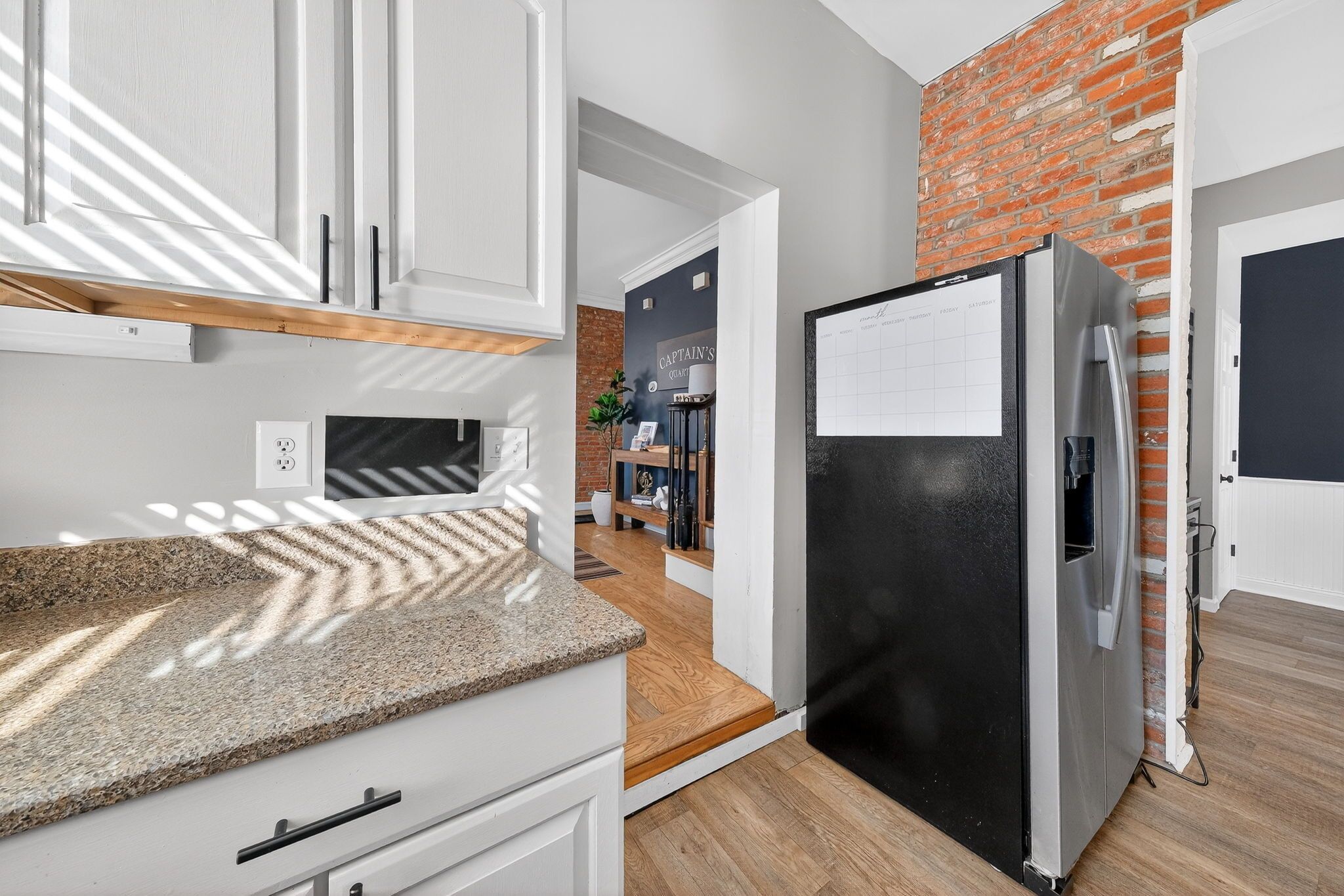 A kitchen with white cabinets, a black refrigerator, and a brick wall.