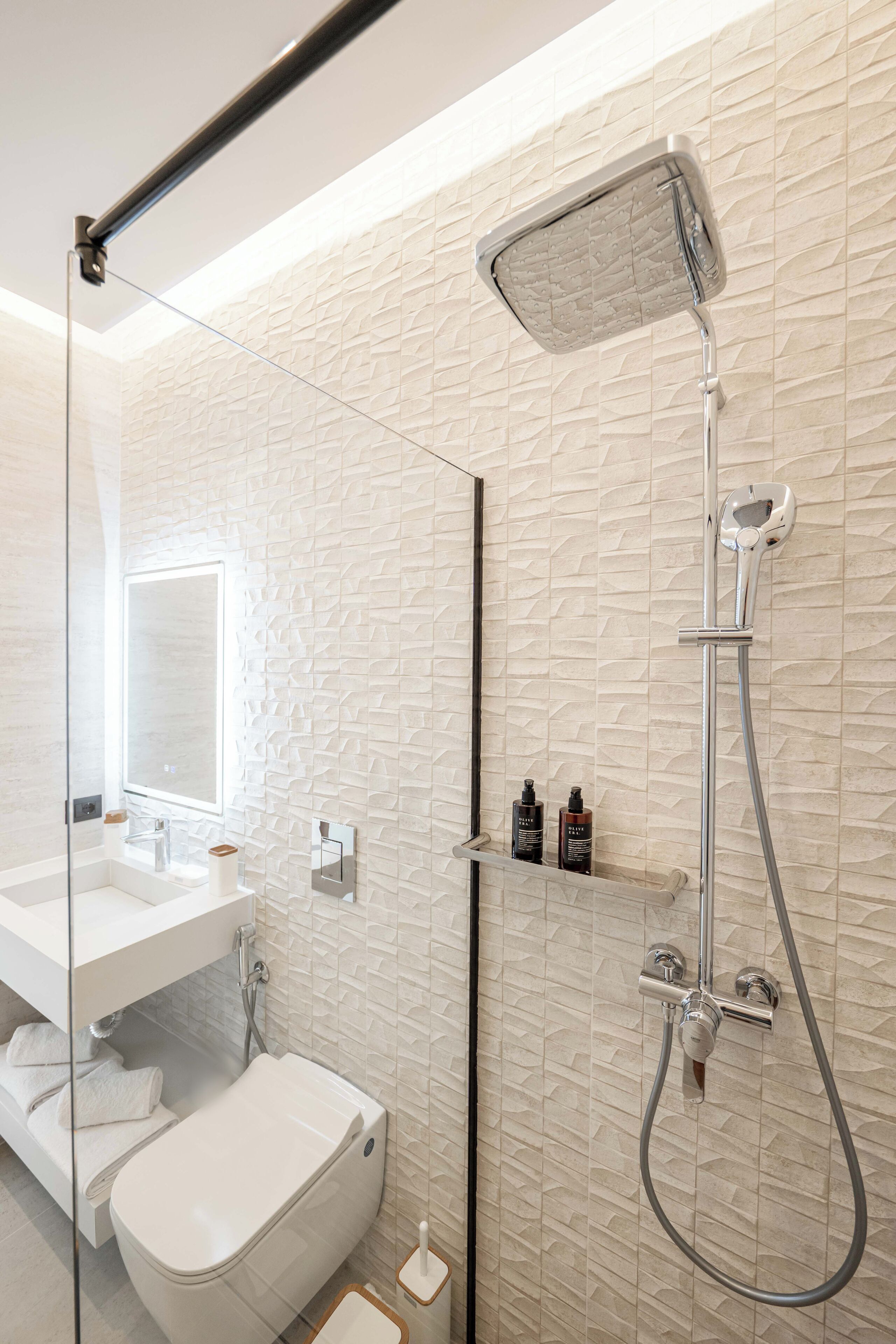 Een moderne badkamer met een glazen douchecabine, toilet en een wastafel met spiegel.