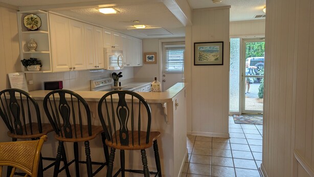 A kitchen with white cabinets, a stove, and a dining area with three chairs. - Beach/Pool Access-Location Location Location! (Hilton Head Island)