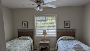 A bedroom with two beds, a ceiling fan, a window with blinds, and a bedside table with a lamp. - Beach/Pool Access-Location Location Location! (Hilton Head Island)