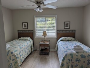 A bedroom with two beds, a ceiling fan, a window with blinds, and a bedside table with a lamp. - Beach/Pool Access-Location Location Location! (Hilton Head Island)