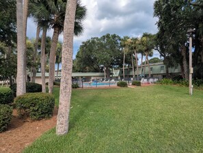 A pool area with lounge chairs, surrounded by palm trees and a fence. - Beach/Pool Access-Location Location Location! (Hilton Head Island)
