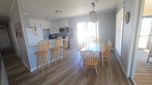 A kitchen with white cabinets, a microwave, and a sink. There is a dining area with a table and chairs. - Saltaire Cottages15: Just Renovated! 3BR Private Beach Access Ocean View Pool! (Kitty Hawk)