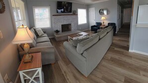 A living room with a fireplace, a ceiling fan, a television, and a sofa. - Saltaire Cottages15: Just Renovated! 3BR Private Beach Access Ocean View Pool! (Kitty Hawk)