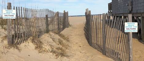 A sandy pathway leading to a wooden building with a sign indicating private beach access for guests only.