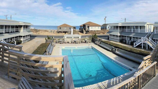 A pool area with a wooden deck, lounge chairs, and a view of the beach and ocean. - Saltaire Cottages15: Just Renovated! 3BR Private Beach Access Ocean View Pool! (Kitty Hawk)