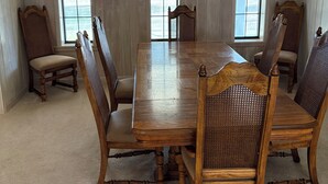 Comedor con mesa de madera y seis sillas, ventanas amplias y una araña.