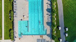 Ein rechteckiger Pool mit Sprungbrett, umgeben von Liegestühlen und einem Parkplatz.
