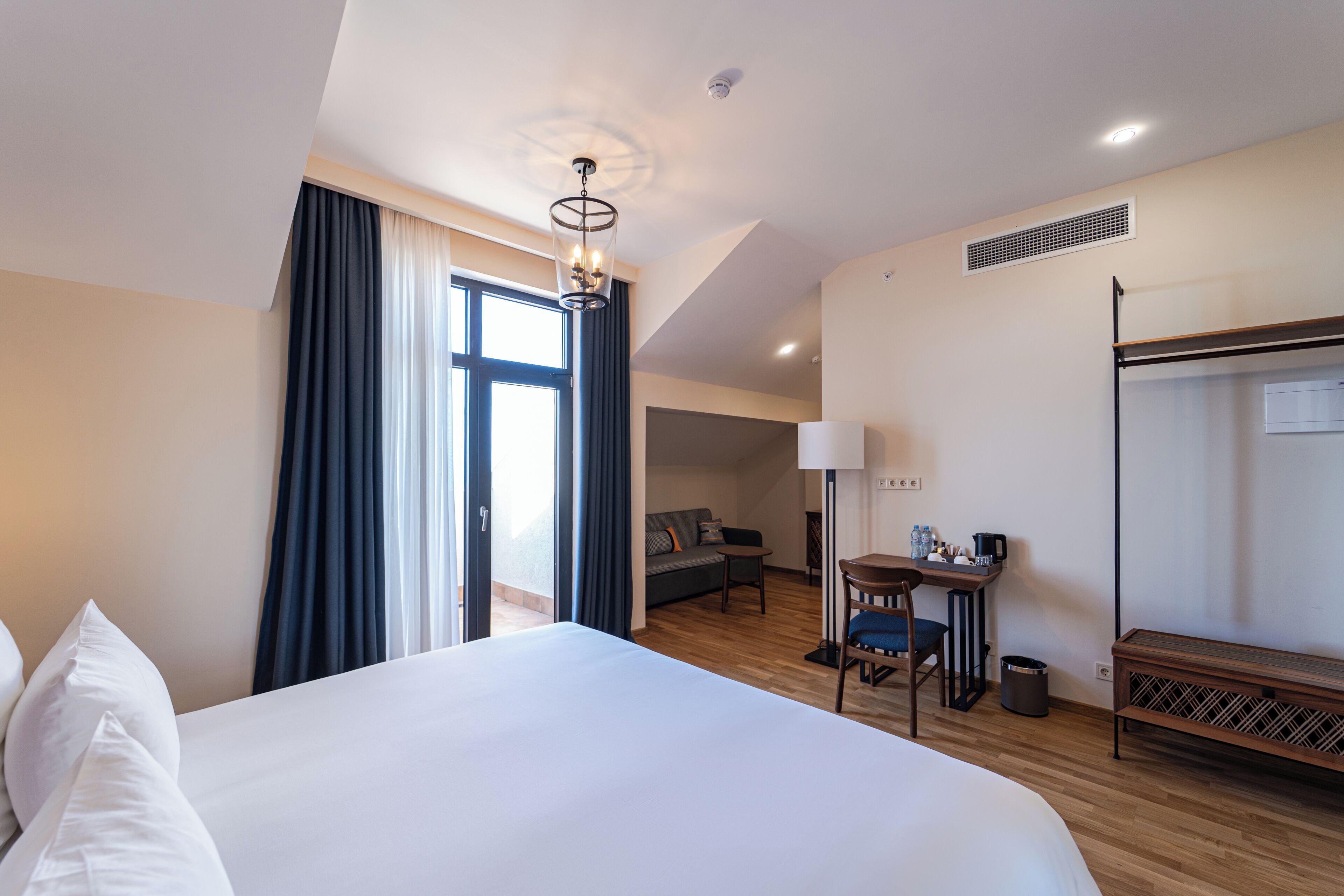 Una habitación de hotel con una cama grande, un escritorio con silla, un sofá y una ventana con cortinas.