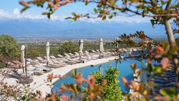 Un espace aménagé au bord de la piscine, avec des chaises longues et des parasols, offrant une vue dégagée sur le paysage urbain et les montagnes en arrière-plan.