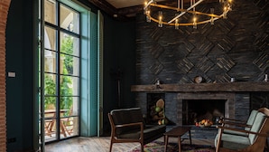 Une pièce avec une cheminée, deux fauteuils, une table basse et une grande fenêtre.