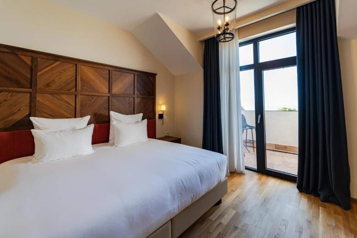 A bedroom with a large bed, a wooden headboard, a balcony with a chair, and a view of the outside.